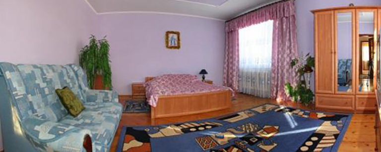 Large cozy bedroom with a bed, sofa, wardrobe, large bright window and a colourful rug on the floor