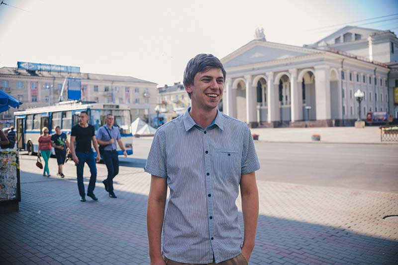 A young man is standing on a sidewalk, in front of a theatre.