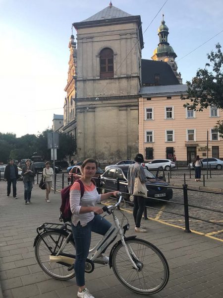 A young woman standing with a bicycle on a sidewalk