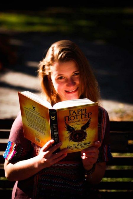 A young woman is reading a book on a park bench.